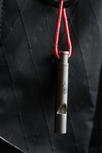 Survival Whistle by Kind Design - titanium whistle on red polycord against black fabric